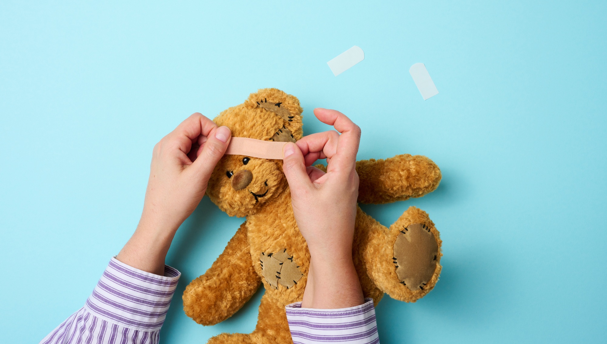 Female hand holds a brown teddy bear and glues a medical adhesive plaster