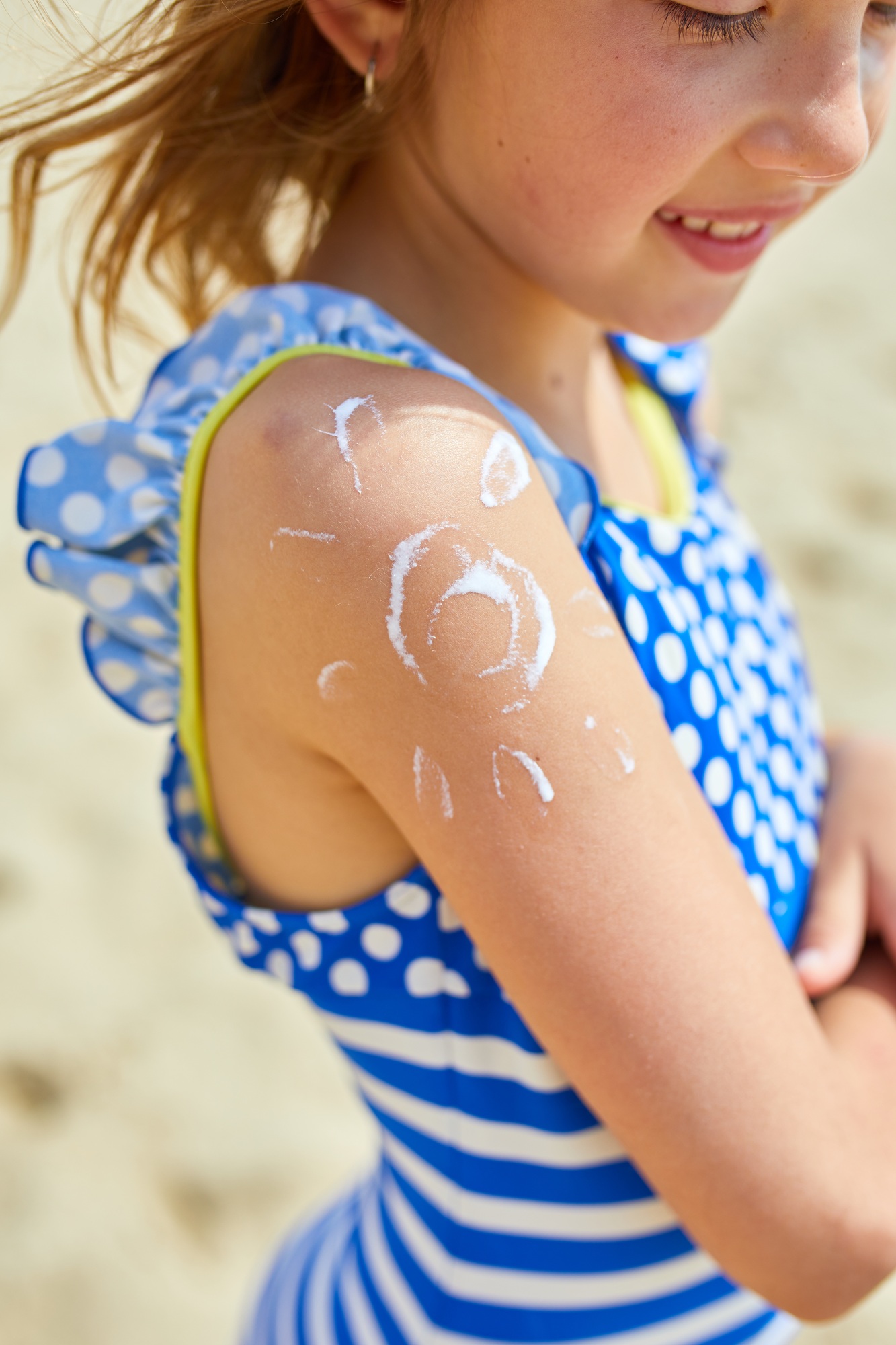 Little girl with applying sunscreen on shoulder in form of the sun standing on the beach