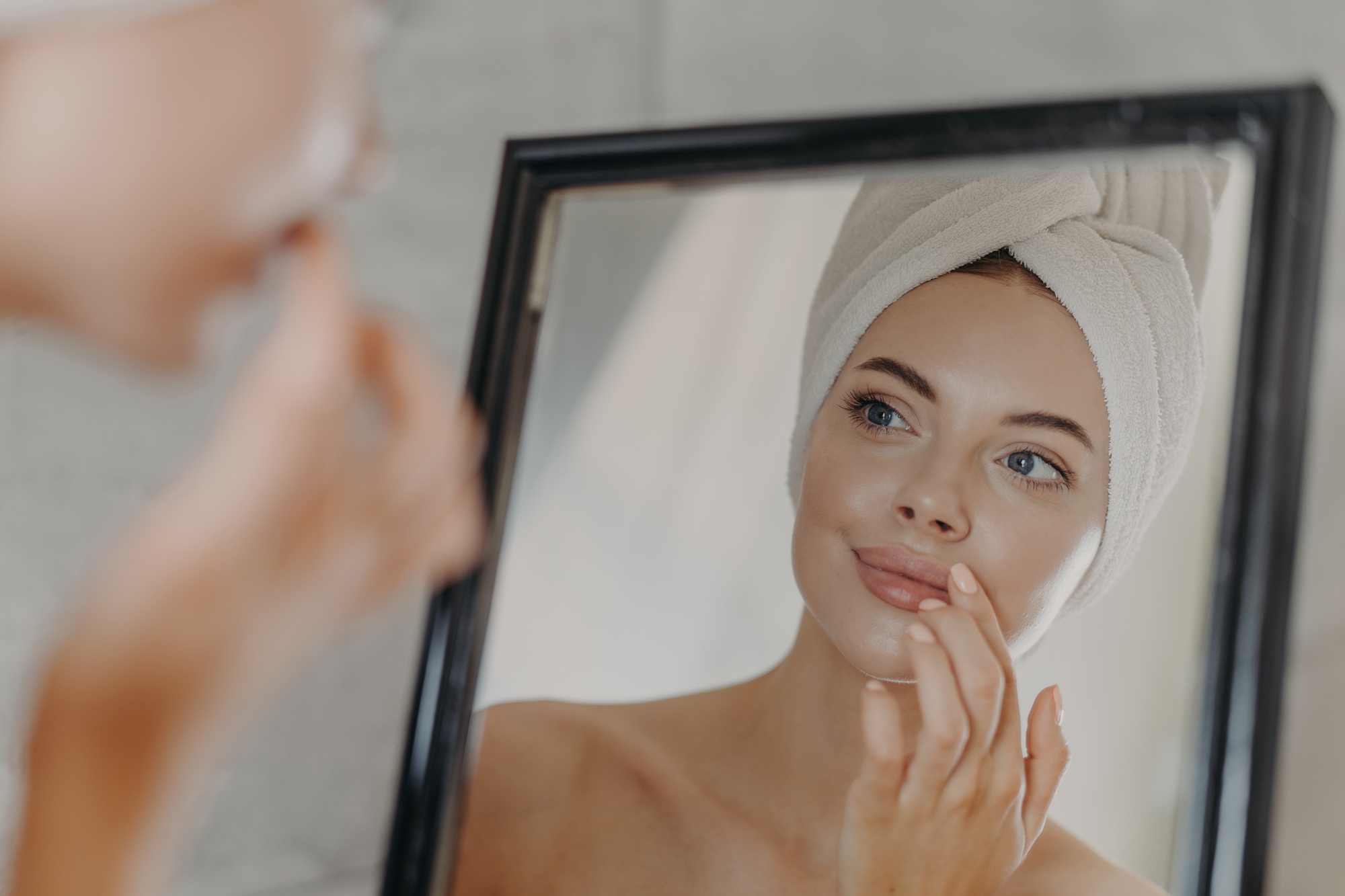 Woman wears minimal makeup, takes care of complexion and lips, looks at herself in mirror