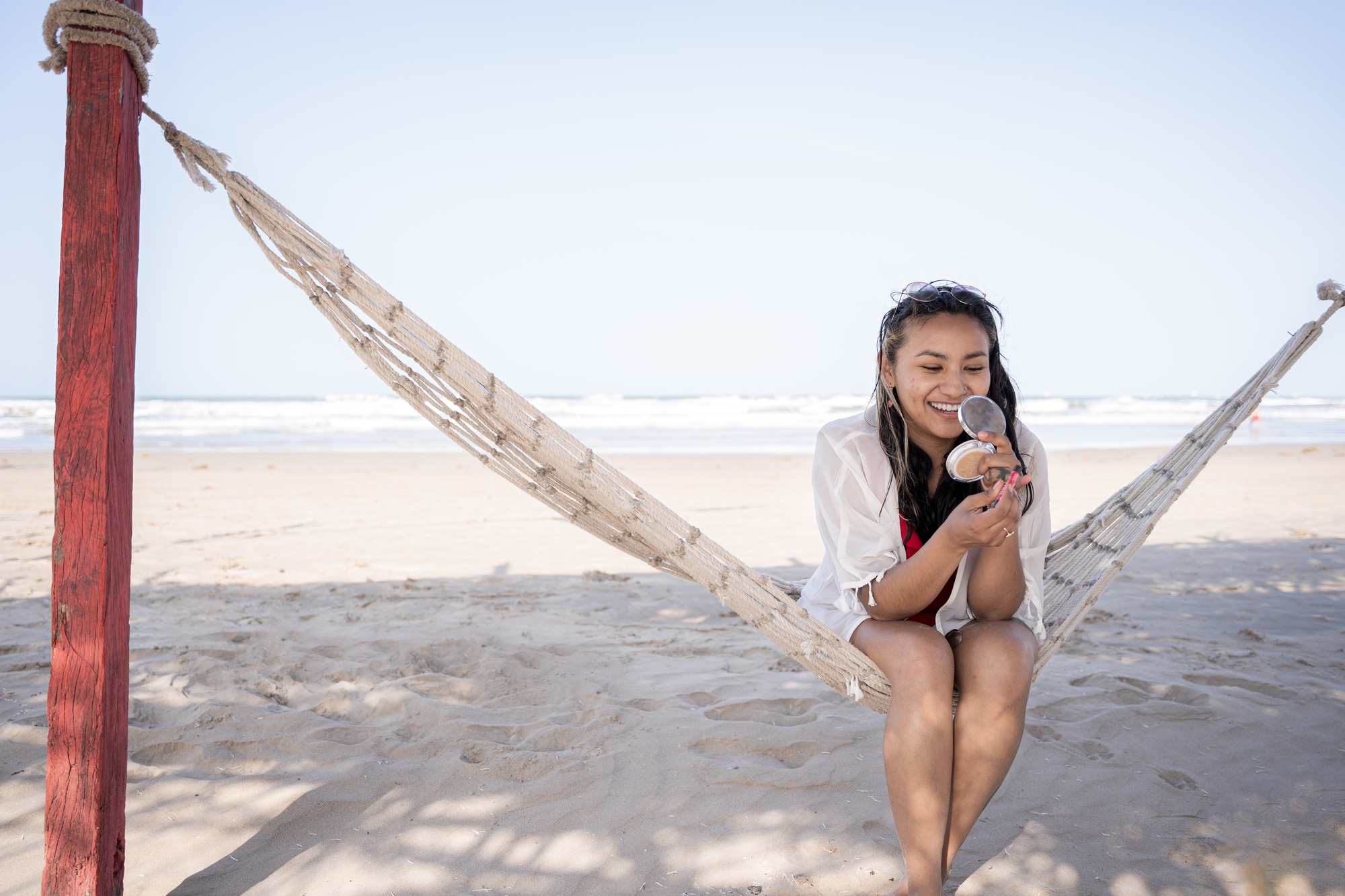 Hispanic woman doing makeup on a hammock at the beach