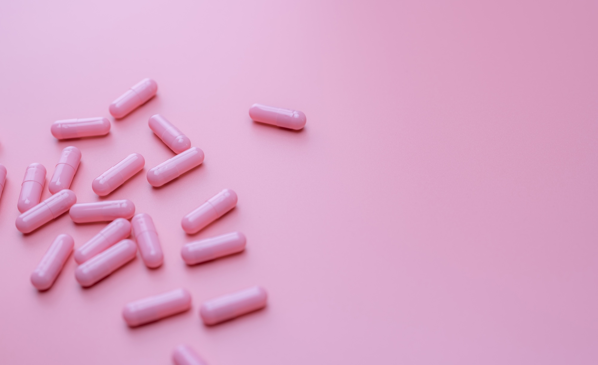 Pink capsules pill spread on pink background. Vitamin and supplement for healthy skin and acne