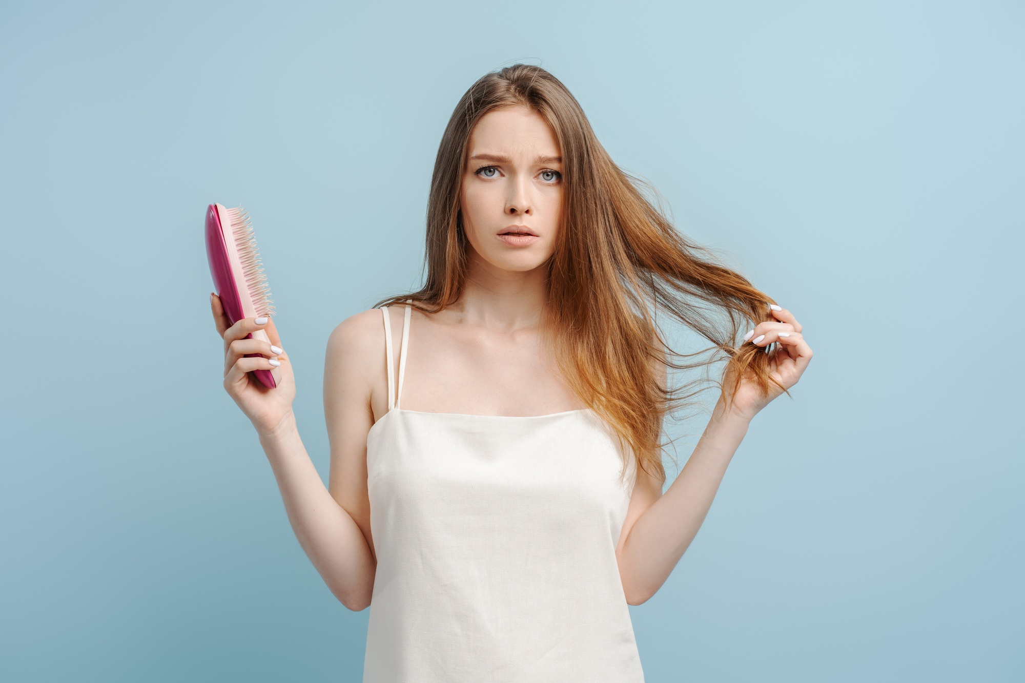 Portrait of sad young woman holding hair brush, hair loss, looking at camera. Concept of hair care