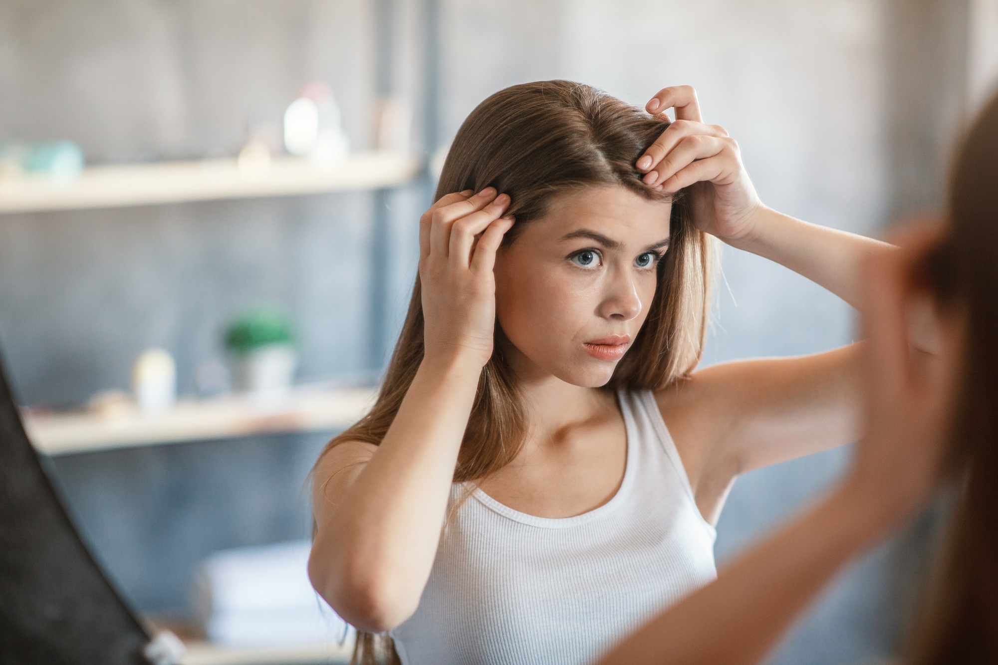 Pretty girl with hair loss problem looking in mirror at home