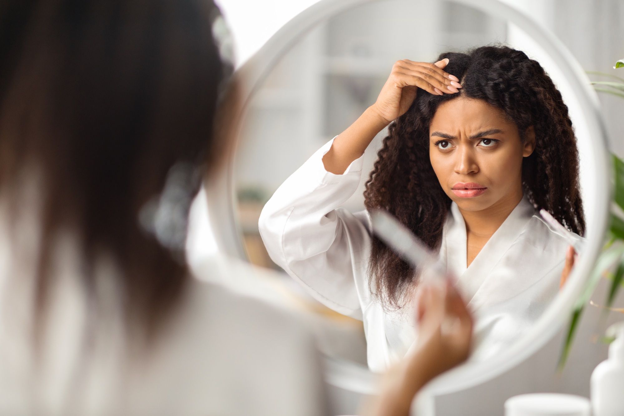 Upset Black Female Looking At Mirror And Touching Her Hair Roots