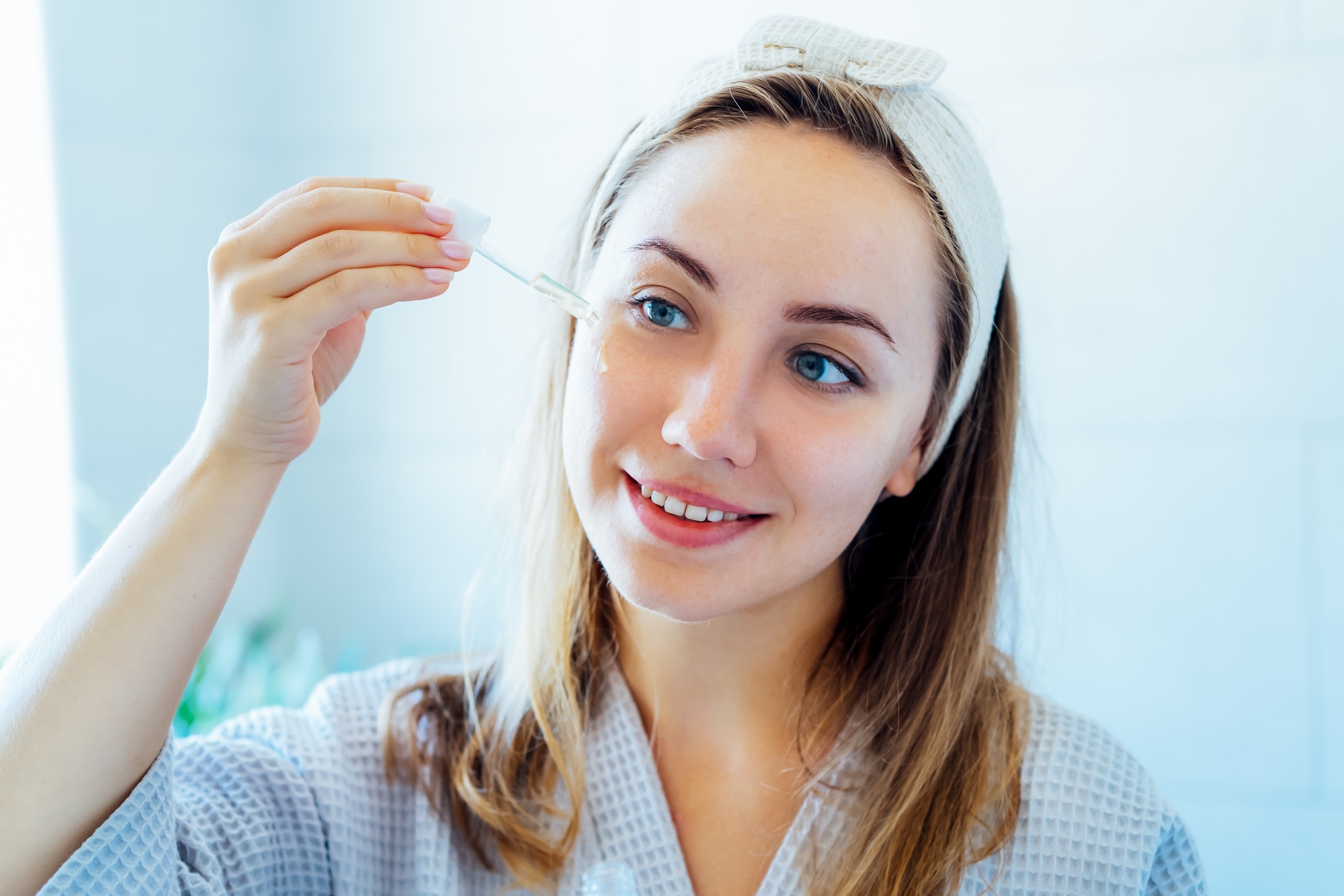 Young woman holding dropper with hyaluronic acid serum close to face. Skin hydrating