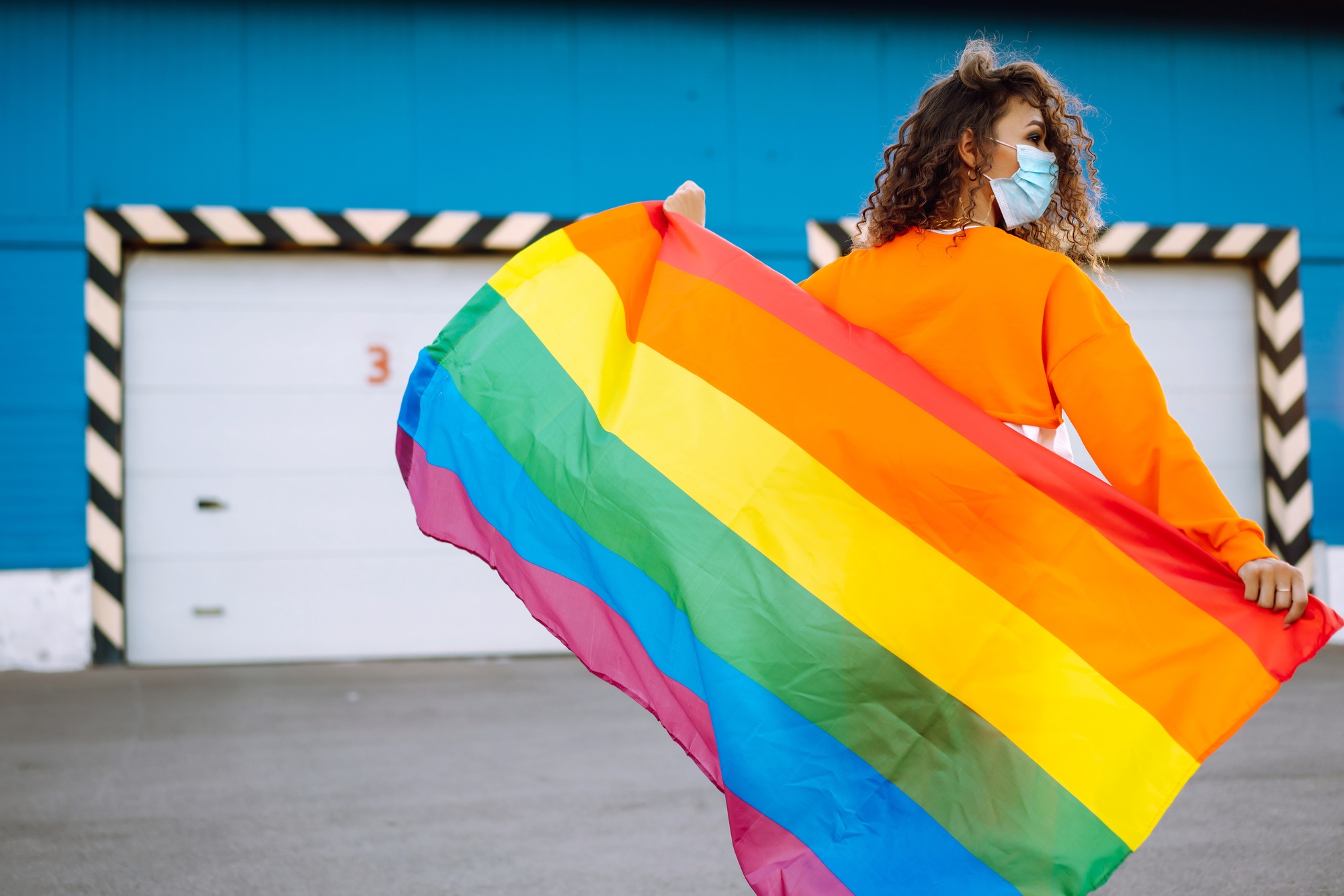 African American lesbian woman with medical face mask posing with lgbt pride flag. Covid-19.