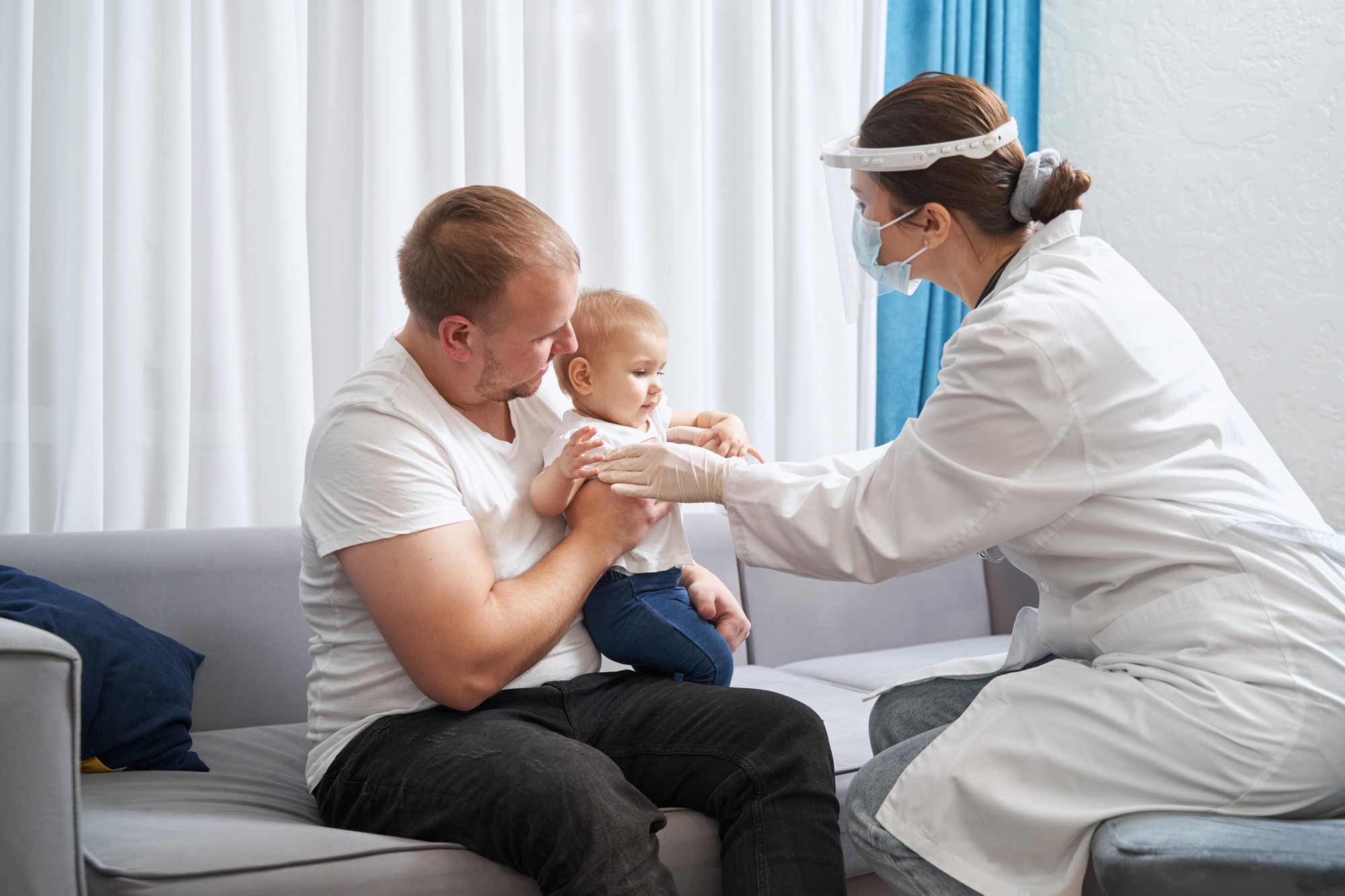 Doctor examining child at home with its father