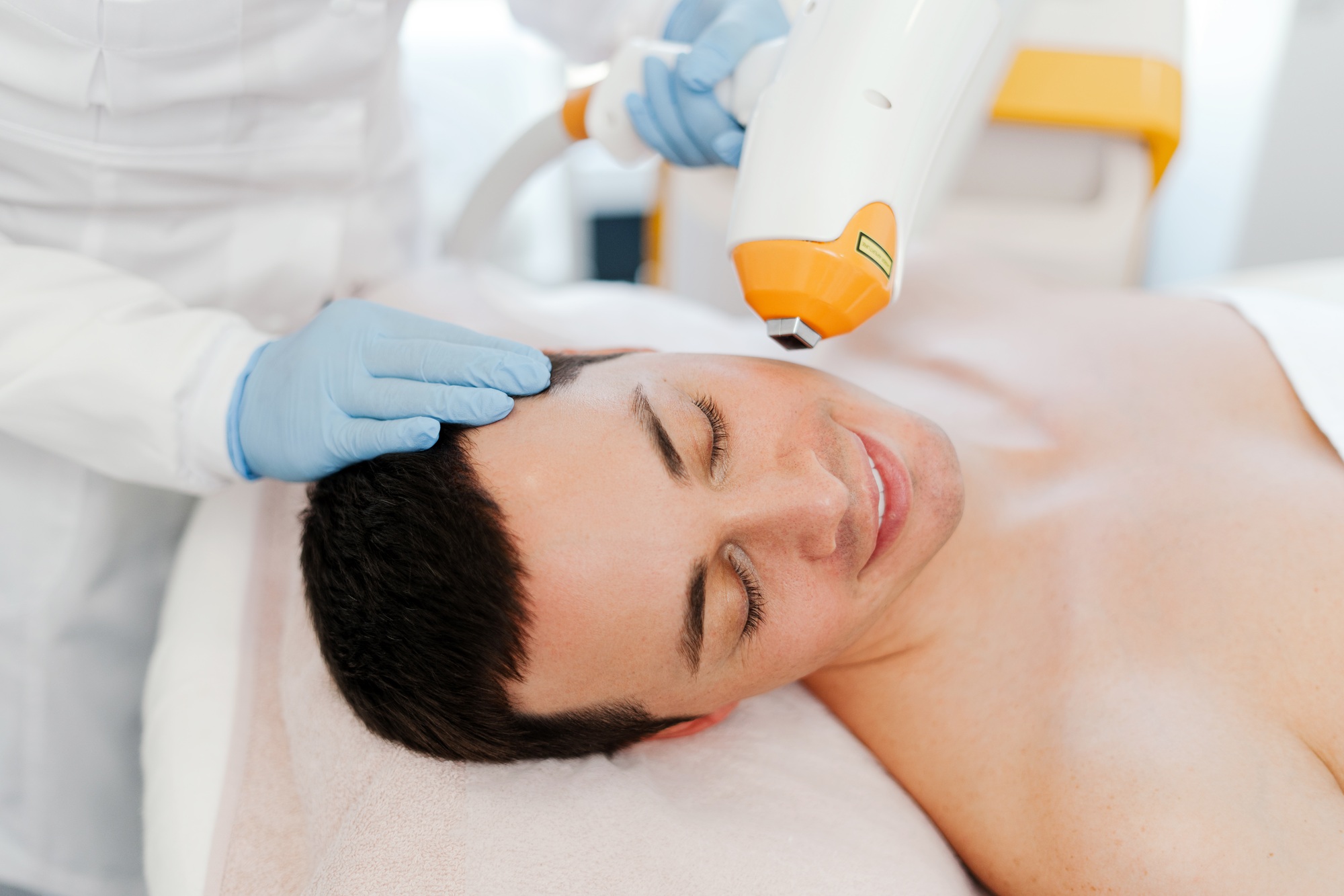 Handsome, young man getting cosmetic procedures, beautician using laser, removing facial hair