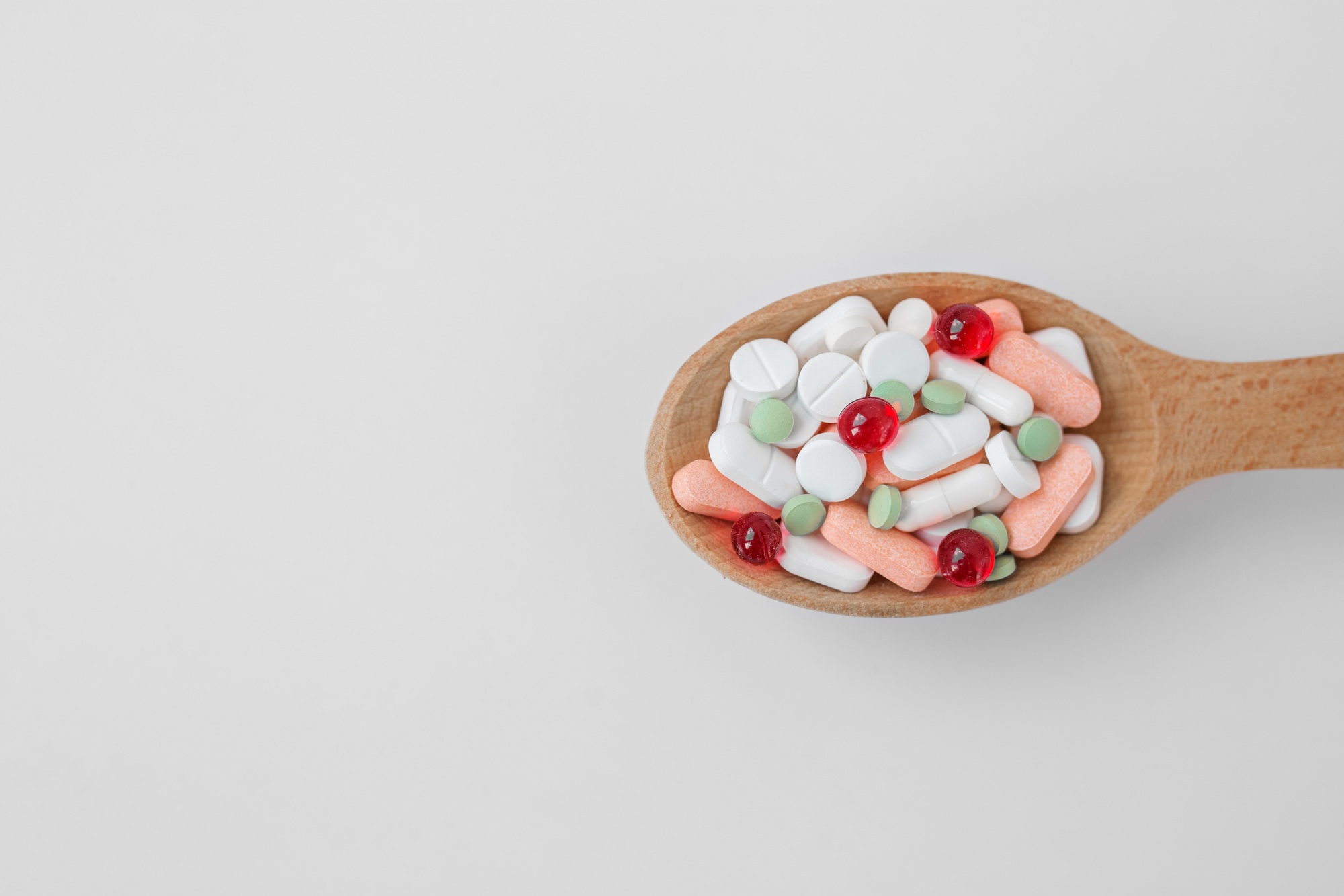 Many different pills in wooden spoon on white background. Copy space. Top view