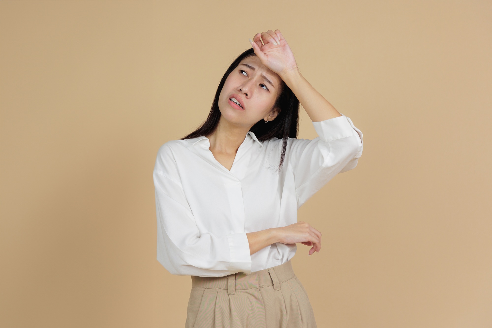 Overheated Woman Wiping Sweat from Forehead, Beige Background