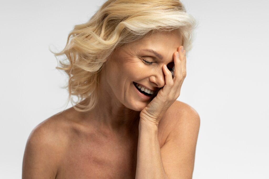 Delightful naked blonde mature woman laughing, isolated over white background. Copy ad space