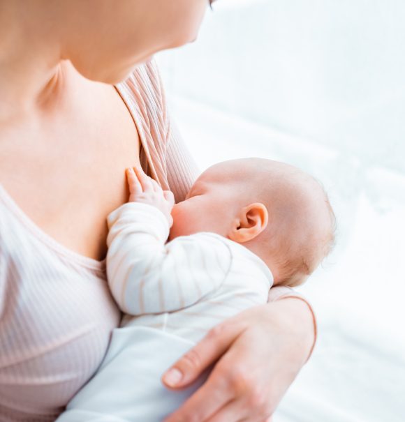 cropped shot of young mother breastfeeding adorable baby at home