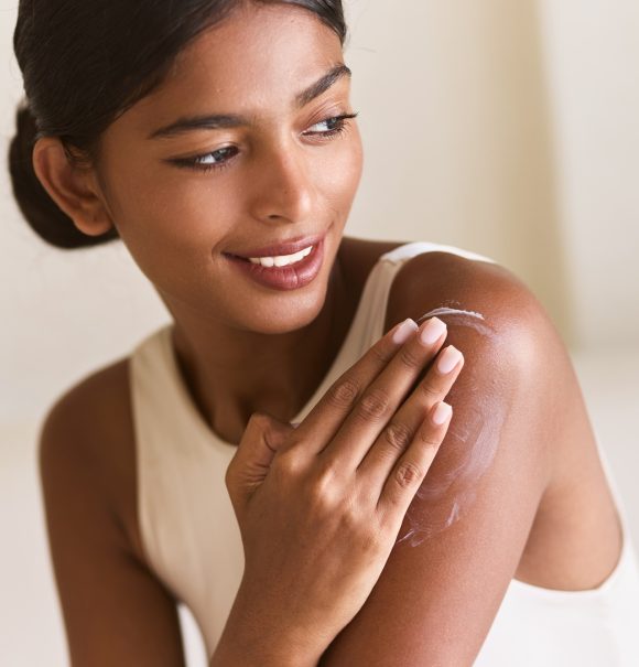 Smiling Woman Applying Hydrating Skincare Cream on Shoulder for Radiant Skin